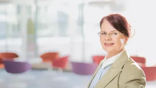 Nainen katsoo kameraan avarassa sisätilassa.