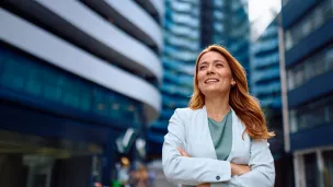 Smiling woman in a blazer stands confidently in a cityscape.